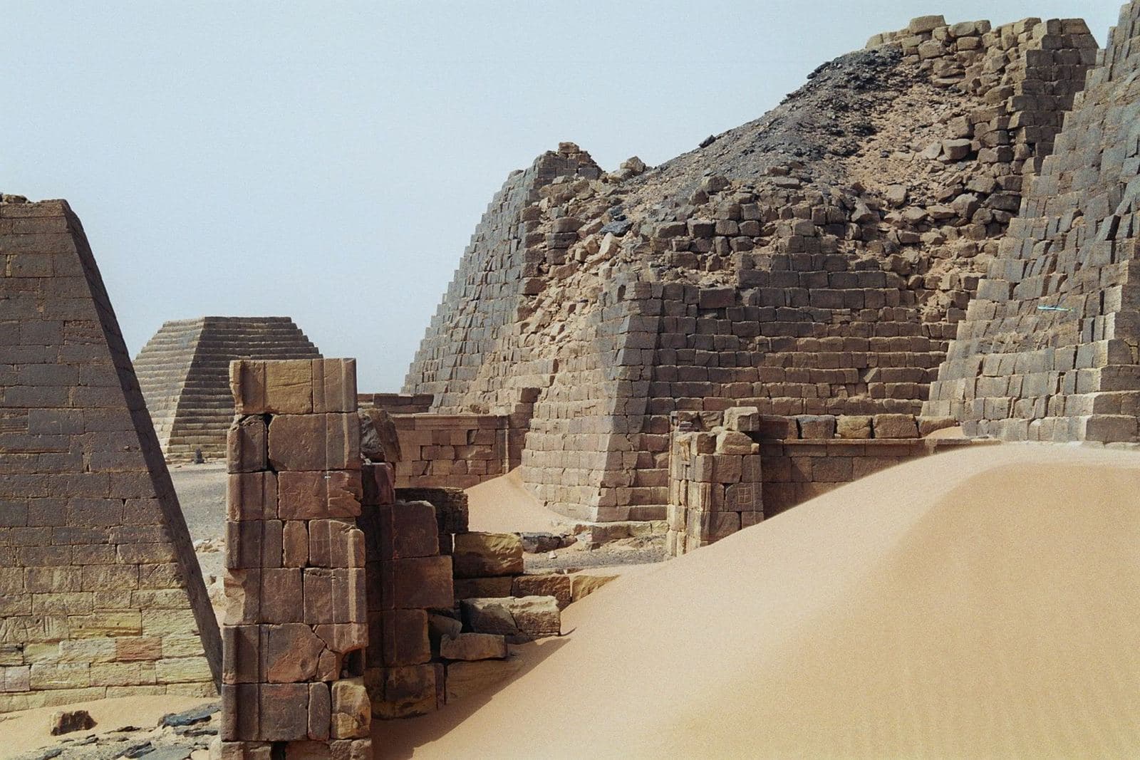 Colour photograph of steep-sided stone pyramids rising from desert sand at Meroë, Sudan
