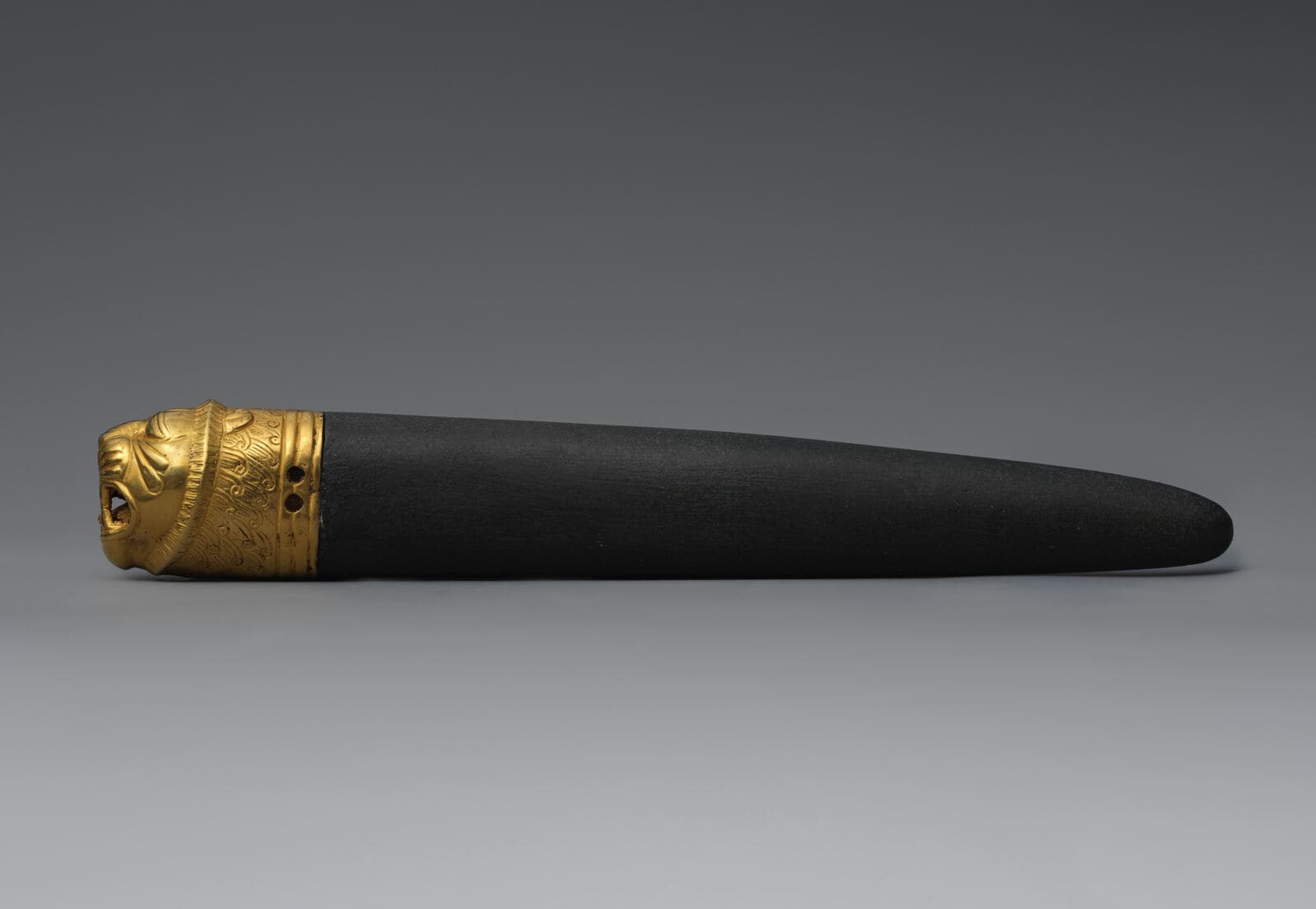 Small carved gold lion's head ornament, mounted in modern times on a dark whetstone