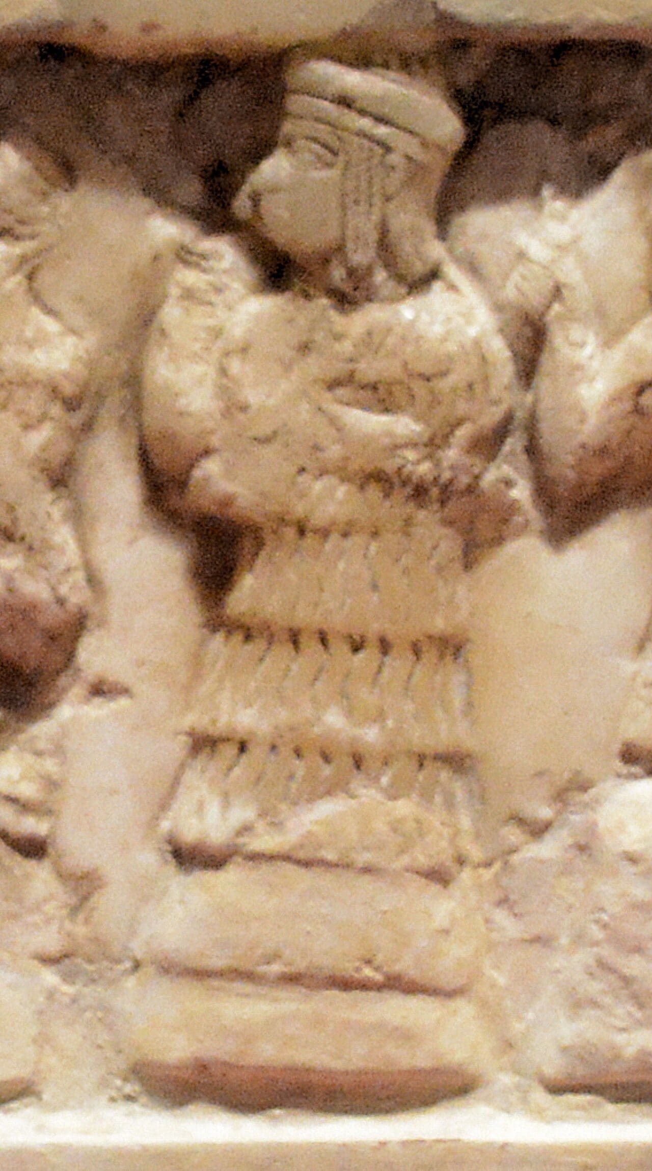 Close crop of a carved calcite disk showing a robed woman in profile with one hand raised in a ritual gesture