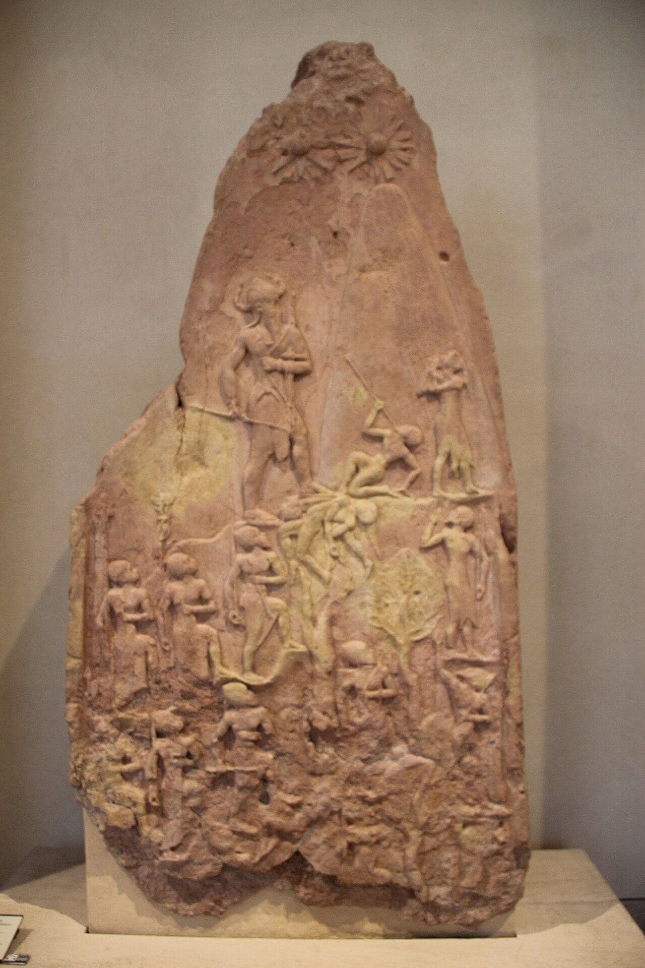 Carved stone stele showing a king climbing a mountain over the bodies of defeated enemies