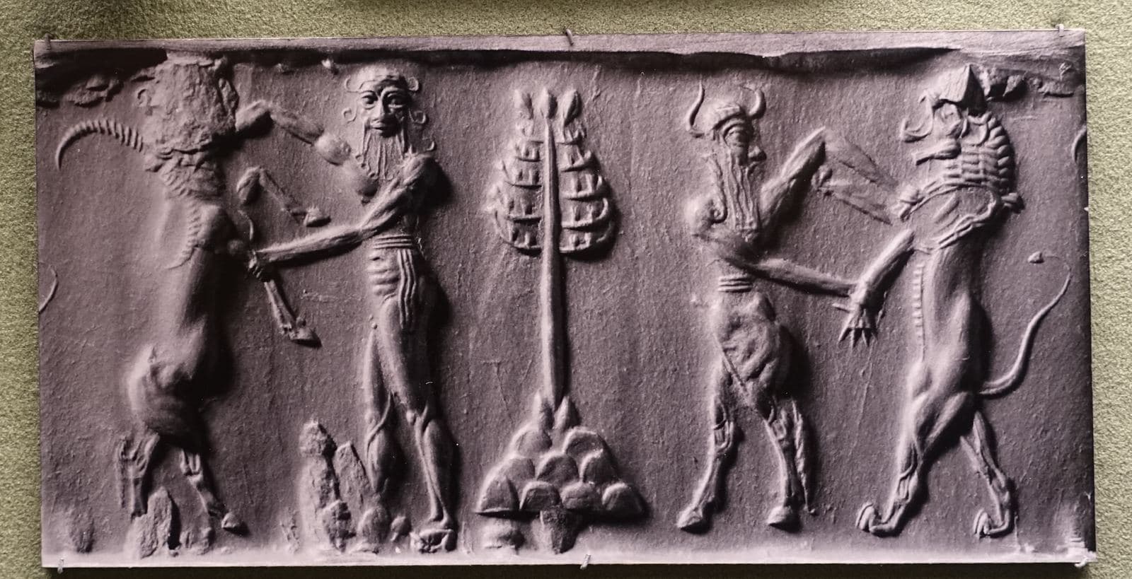 Rectangular clay impression from a cylinder seal showing a naked bearded hero wrestling a horned water buffalo and a bull-man grappling with a lion, a plant between them