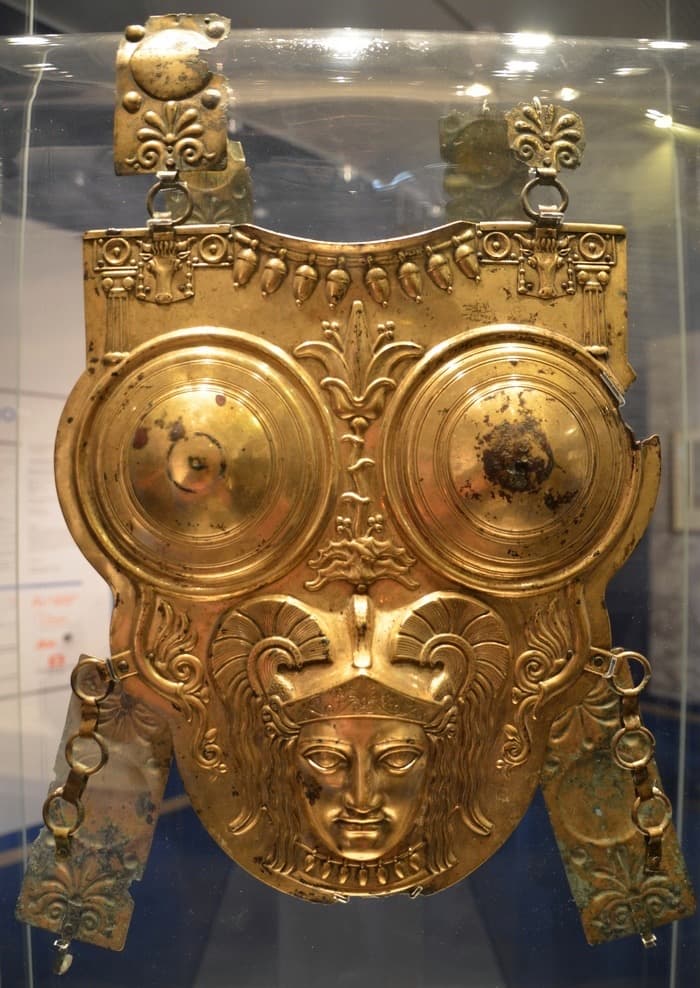 Gilded bronze breastplate decorated with three raised discs, mounted upright in a museum display