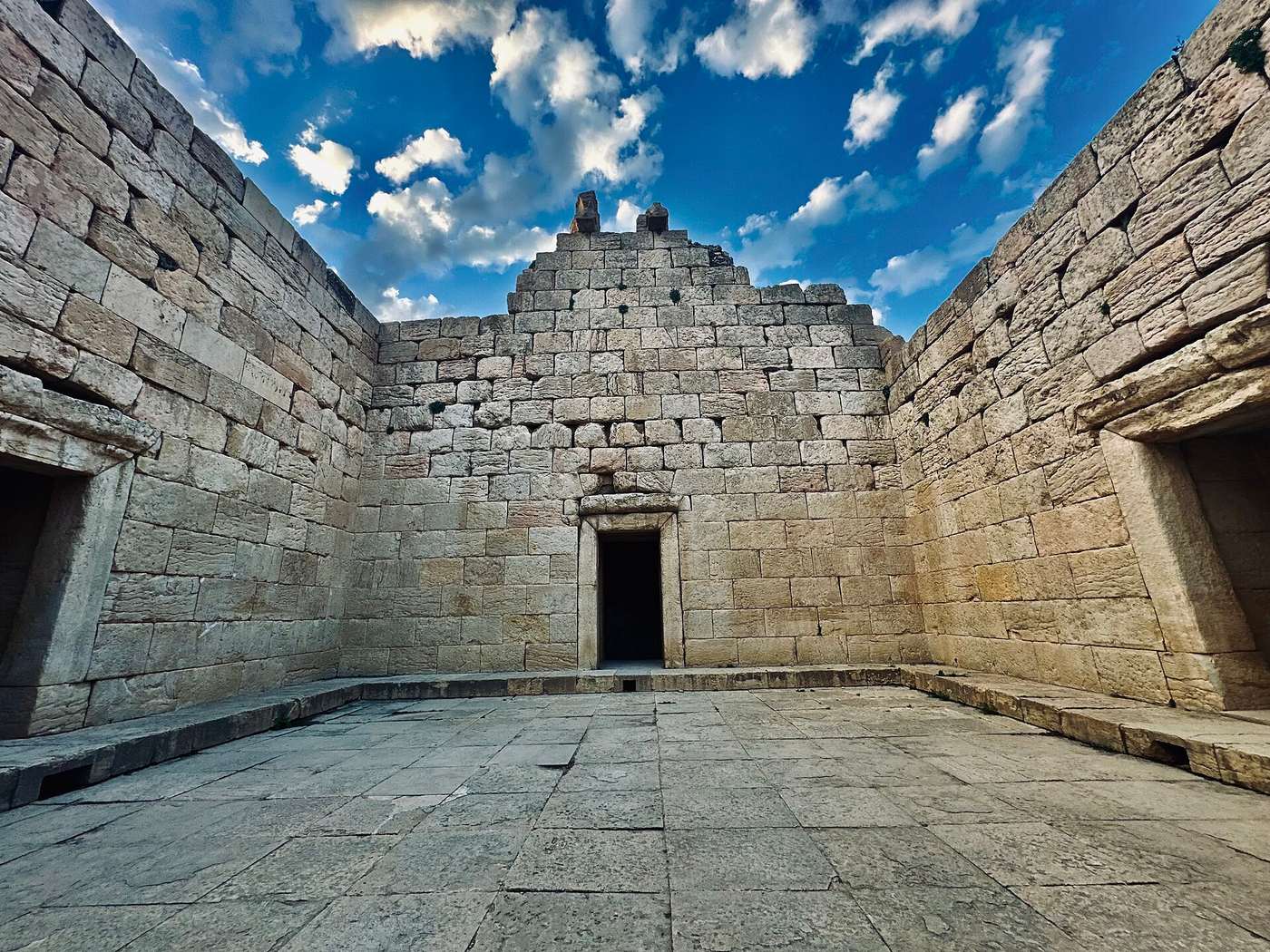 Weathered stone ruins of an ancient temple complex, broken columns and foundation walls under an open sky