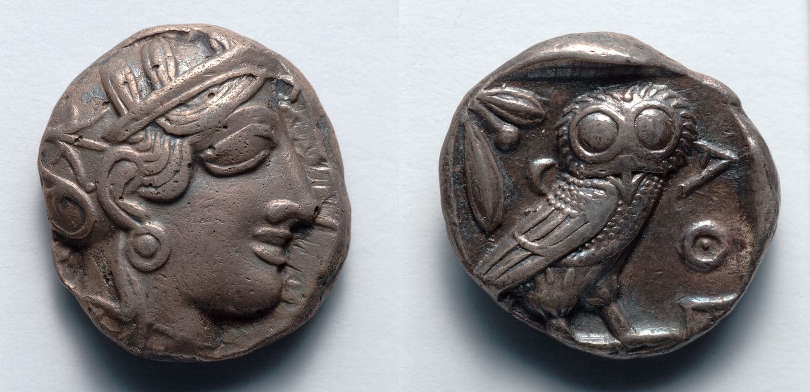 Ancient Greek silver coin showing an owl facing forward beside an olive sprig and a crescent moon