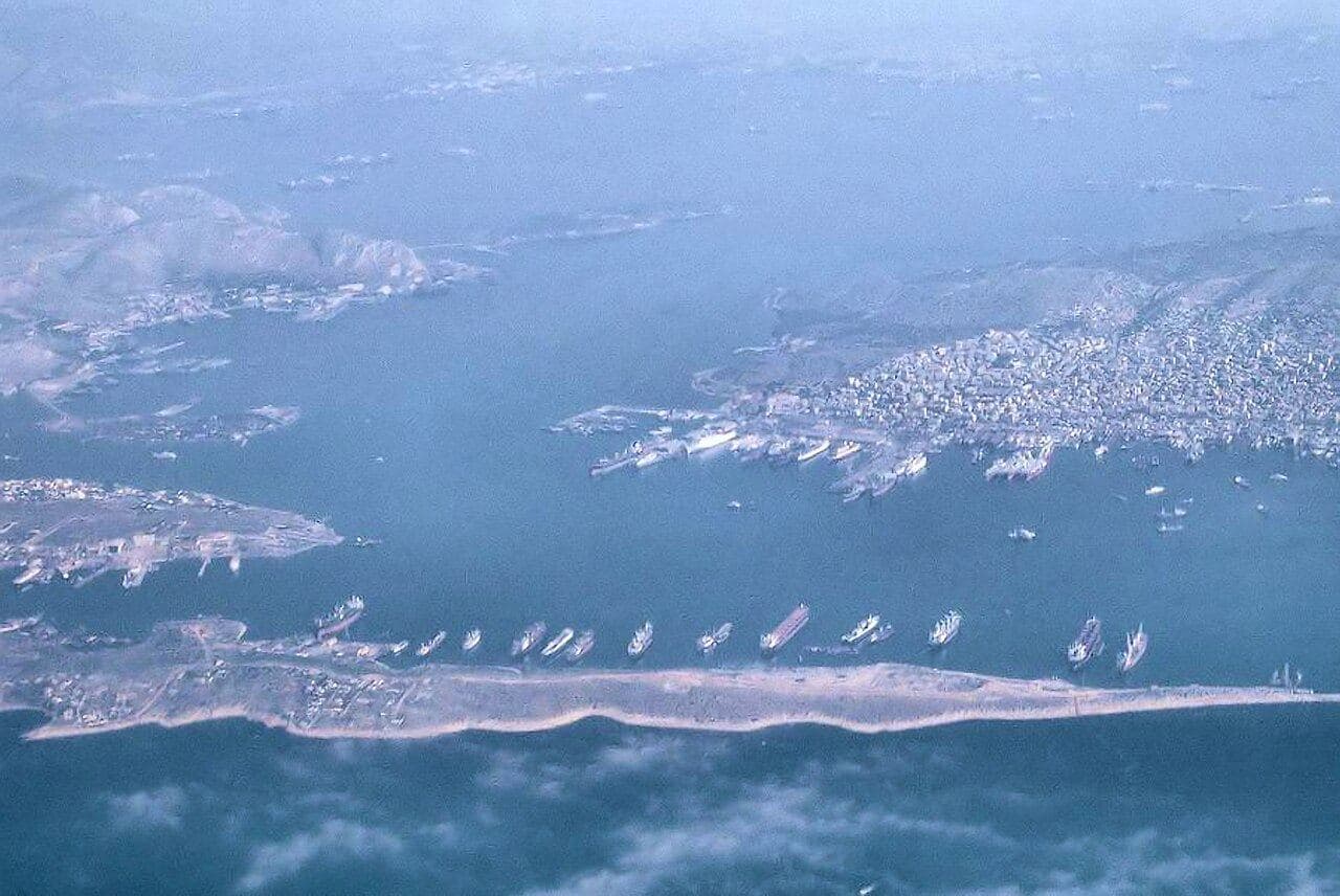 Aerial photograph of a narrow sea strait between an island and the mainland, dotted with ships