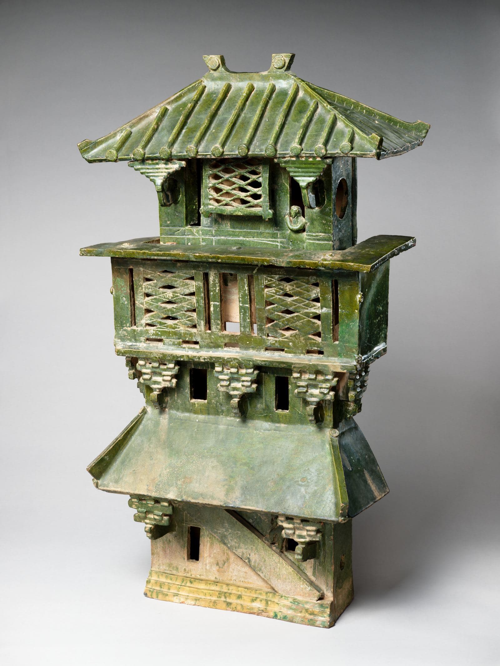 Tall multi-story earthenware model of a fortified watchtower with green glaze, mounted on a museum stand