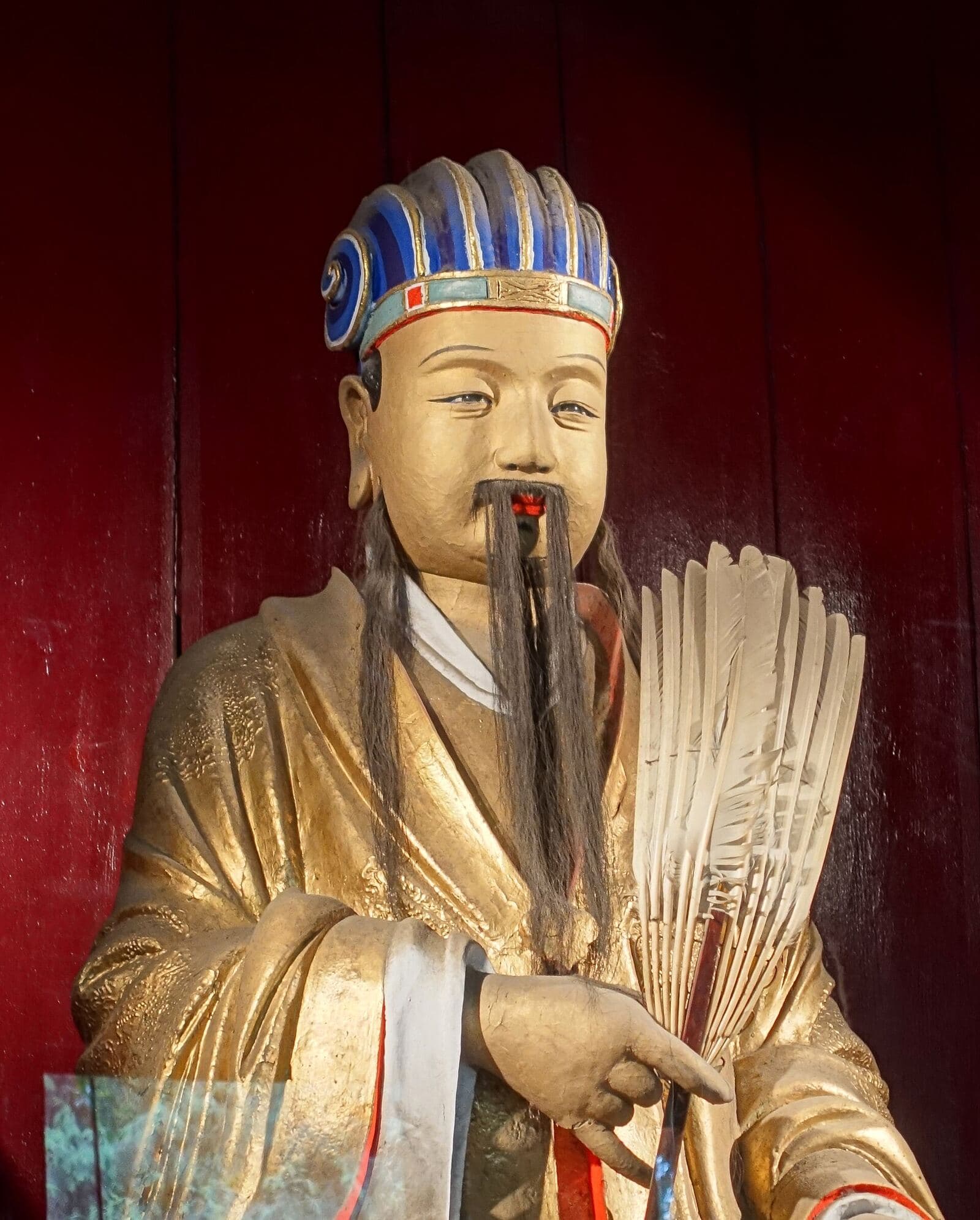 Seated statue of Zhuge Liang in flowing robes, holding a feather fan, inside a temple hall